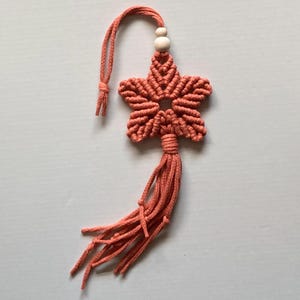 May include: A coral-coloured macrame star with a white bead and a long tassel.