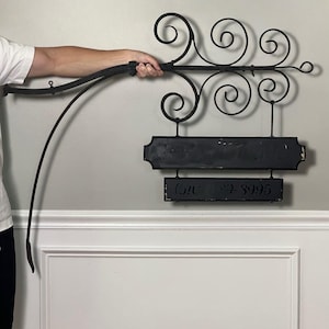 May include: A black wrought iron hanging sign featuring decorative scrollwork at the top. The sign consists of two rectangular panels suspended from the metal frame. The top panel is larger, and the bottom panel displays the text (610) 829-3995.