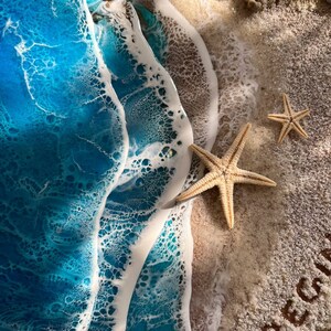 Closeup view of beautiful ocean beach resin wall art resting on a wooden base with customizable names or messages on the sand.