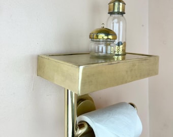 Könnte beinhalten: Toilettenpapierhalter aus Messing mit einem Regal und zwei kleinen Glasbehältern mit goldenen Deckeln. Das Regal ist an der Wand befestigt und der Toilettenpapierhalter ist am Regal befestigt.