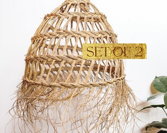 May include: A set of two natural woven pendant lights with a fringe detail. The lights are made of natural materials and have a rustic, bohemian style. The text "SET OF 2" is visible on the image.