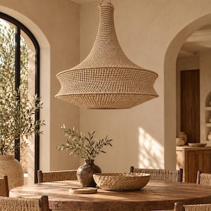 May include: A large, bell-shaped pendant light fixture crafted from woven tan natural fibers, featuring a wide, textured body that tapers toward the top, suspended by a thin cord from the ceiling in a neutral-toned room.