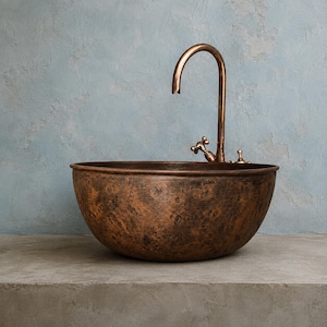 May include: A round, hammered copper vessel sink with a dark, mottled patina finish. A tall, curved copper faucet with two cross-handle knobs is positioned directly behind the basin, featuring a matching metallic finish and a high-arched spout.