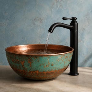 May include: A round vessel sink with a hammered copper interior and a weathered teal and copper exterior finish. A tall, matte black faucet stands beside the basin, with a steady stream of water flowing from the spout into the filled sink bowl.
