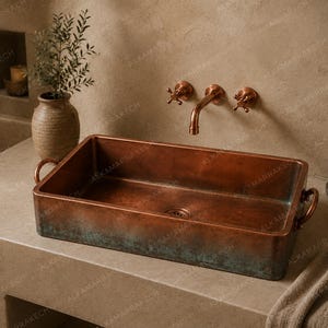 May include: A rectangular copper sink with side handles, featuring a weathered patina finish with green oxidation near the base. The sink is paired with a wall-mounted copper faucet with two cross-handle valves, creating a cohesive metallic look.