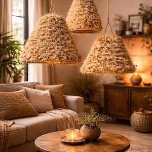 May include: Three pendant lights with conical shades made of a textured, light brown material hang from the ceiling. The room features a neutral color palette with a sofa, coffee table, and decorative items.