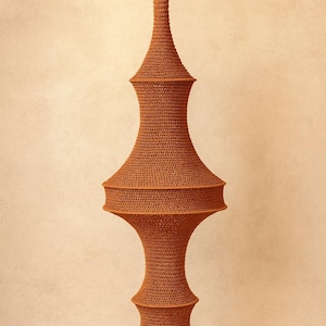 May include: A tall, rust-colored, crocheted hanging lamp shade with a complex, multi-tiered silhouette. The structure features a narrow neck, a wide central section, and a flared base, all crafted from a dense, uniform yarn stitch pattern.