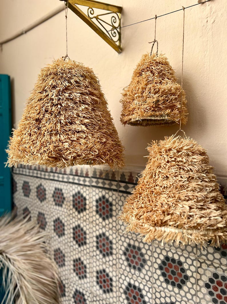 May include: Three hanging pendant lights with a natural, textured, straw-like material. The lampshades are cone-shaped and suspended from a wire. The background features a patterned tile wall and a decorative metal bracket.