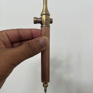 Puede incluir: Un pequeño tubo de cobre y latón con una válvula de resorte y un llavero. El tubo mide aproximadamente 15 cm de largo y tiene un acabado marrón oscuro.