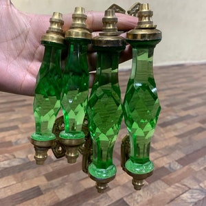 May include: Set of four green glass cabinet knobs with brass accents. The knobs have a faceted design and are attached to brass plates.