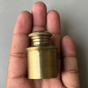 May include: A small, gold-colored metal jar with a decorative lid. The jar is about 2 inches tall and has a smooth, rounded body.