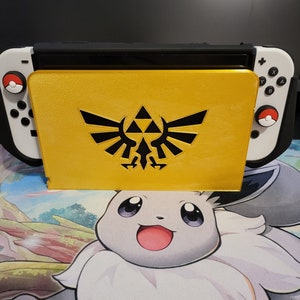 May include: A yellow Nintendo Switch case with a black Triforce design. The case is closed and the console is visible in the background.