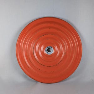 Peut inclure: Plaque de poids ronde et orange avec des rainures circulaires concentriques. Le centre comporte un insert métallique argenté avec le mot "welder". Conçu pour l'haltérophilie et l'exercice. Diamètre d'environ 30 cm.