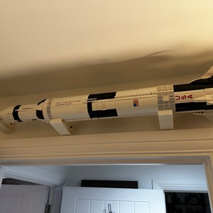 May include: A large model rocket, predominantly white with black accents, is mounted on a wall. The rocket features the word "USA" and an American flag. The model is displayed above a doorway, showcasing its impressive size and detail.