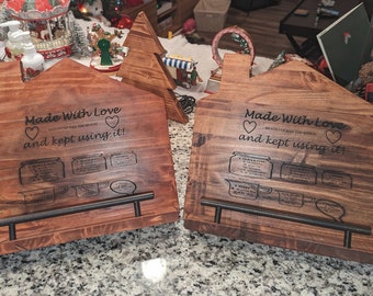 May include: Two wooden recipe holders shaped like houses with the text "Made With Love and kept using it!"  Each holder has a metal bar for holding recipes and a series of engraved jars and measuring cups.