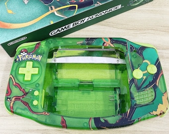 May include: A green Game Boy Advance console and matching box. The console features a transparent green shell with a Pokemon design. The box and console have a green and gold color scheme with the text "GAME BOY ADVANCE" and "Pokemon".