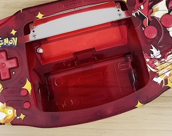 May include: A red Game Boy Advance SP with a Pokemon design. The console has a clear red shell with a Pokemon character on the front and a red dragon on the back. The console has a silver cartridge slot and a red screen.