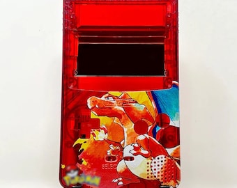 May include: A red transparent Game Boy Color with a custom Charizard design. The console is on a black stand. The console has a black screen and a red button.