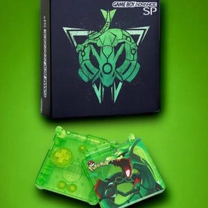 May include: A green Game Boy Advance SP console with a clear green shell and a Pokemon design. The console is open and the top screen shows a green Pokemon character with a red mouth.