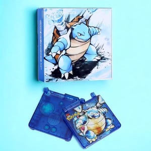 May include: A blue Game Boy Advance SP console with a Blastoise design. The console is open and the top screen is showing a close-up of Blastoise. The bottom screen is showing the Pokemon logo.