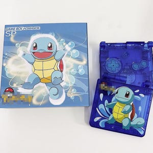 May include: A blue Game Boy Advance SP console with a Squirtle design. The console is closed and the front features a cartoon image of Squirtle surrounded by bubbles. The text "GAME BOY ADVANCE SP" is printed on the front of the console.