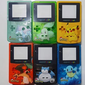 May include: Six different colored Game Boy Color shells with Pokemon designs. The shells are green, yellow, orange, black, blue, and light blue. Each shell has a different Pokemon character on it. The text "GAME BOY COLOR" and "POKEMON" are printed on each shell.