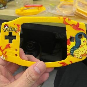 May include: Yellow and red Nintendo Game Boy Advance SP console with a Pokemon design. The console features a screen, buttons, and a Pokemon character on the front.