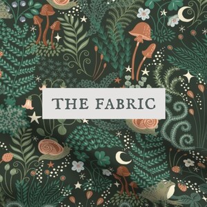 Op de afbeelding: Een donkergroene stof met een herhalend patroon van bruine paddenstoelen, slakken, kikkers, aardbeien, varens en kleine witte sterren en maansikkels. Een wit rechthoekig label met de tekst THE FABRIC is in het midden van de afbeelding geplaatst.