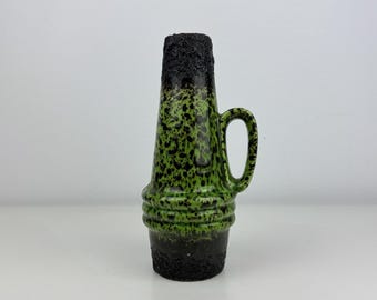 May include: A ceramic pitcher featuring a tapered body with a textured black base and rim. The central section displays a vibrant green glaze with a black speckled pattern. It includes a single curved handle and three horizontal ridges.