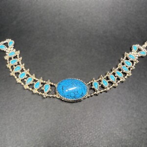 May include: A silver bracelet with a large turquoise stone and smaller turquoise stones in a teardrop shape.