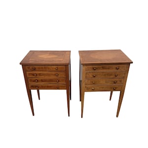 Peut inclure: Deux tables de chevet en bois avec quatre tiroirs chacune. Les tables sont de couleur marron clair avec une incrustation décorative sur le dessus. Les tiroirs ont de petits boutons ronds. Les tables ont des pieds fins et effilés.