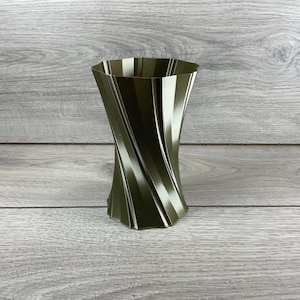 Puede incluir: Un jarrón de color verde oscuro y blanco a rayas con un diseño retorcido. El jarrón está hecho de un material liso y brillante.