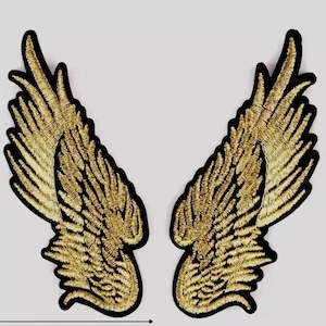 May include: A pair of gold embroidered angel wings with black outlines. The wings are symmetrical and have a detailed design.