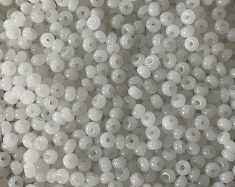 May include: A close-up shot of a pile of small, round, white beads. Each bead has a hole running through the center. The beads are uniform in size and shape, creating a smooth, textured surface. Ideal for jewelry making and crafts.