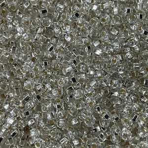 May include: A close-up view of a large quantity of small, clear glass beads with silver accents. The beads are round and have a slightly irregular shape.