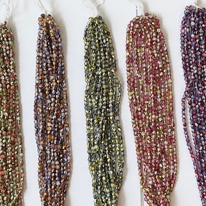 May include: Assortment of 12 strands of iridescent glass seed beads. Each strand is approximately 18 inches long and features a variety of colours, including blue, green, purple, and gold.