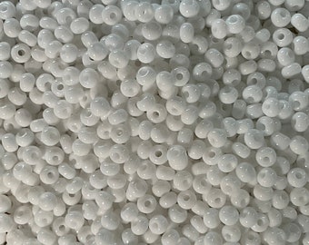 May include: A close-up image of a large quantity of white seed beads. The beads are round and have a small hole in the center.