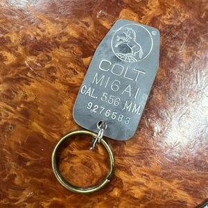 May include: A silver metal keychain with a Colt M16A1 logo and the text "CAL. 5.56 MM. 9276583".