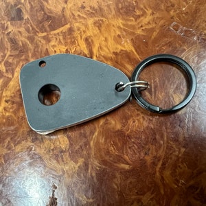 May include: A silver key chain with a black metal ring. The key chain has a round hole in the center and a smaller hole on the top.