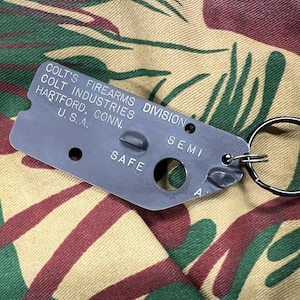 May include: A black metal keychain with the text "Colt's Firearms Division Colt Industries Hartford, Conn. U.S.A." and the words "Safe" and "Semi" on it.