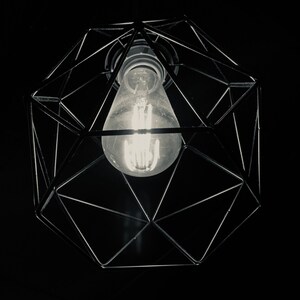 Könnte beinhalten: Eine schwarze geometrische Leuchte mit einer klaren Glühbirne, die von der Decke hängt.