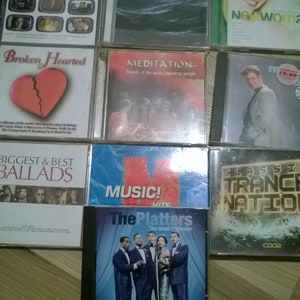 Puede incluir: Una colección de 10 discos compactos (CD) con varios géneros musicales. Los CD están dispuestos en tres filas, con los títulos visibles. Los títulos incluyen "BRIT Album of the Year", "Broken Hearted", "Biggest & Best Ballads", "Meditation Sounds of the Native American People", "Music! The Platters The Great Pretender", "New Woman", "Classic Trance Nation", y más.