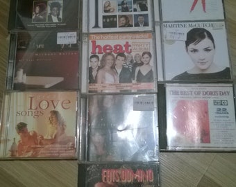 May include: A collection of 10 compact discs (CDs) with various music genres, including love songs, classical music, party music, and the best of the 60s. The CDs are arranged in two rows, with the titles and artists visible. The CDs are all in jewel cases with colorful artwork.