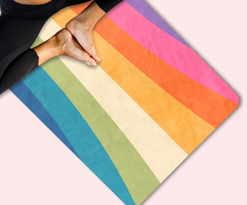 May include: A rainbow yoga mat with a vintage design. The mat has stripes of purple, pink, orange, yellow, green, blue, and white.