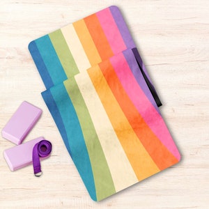 May include: A rainbow yoga mat with a purple strap and two purple yoga blocks. The mat has a faded, vintage look.