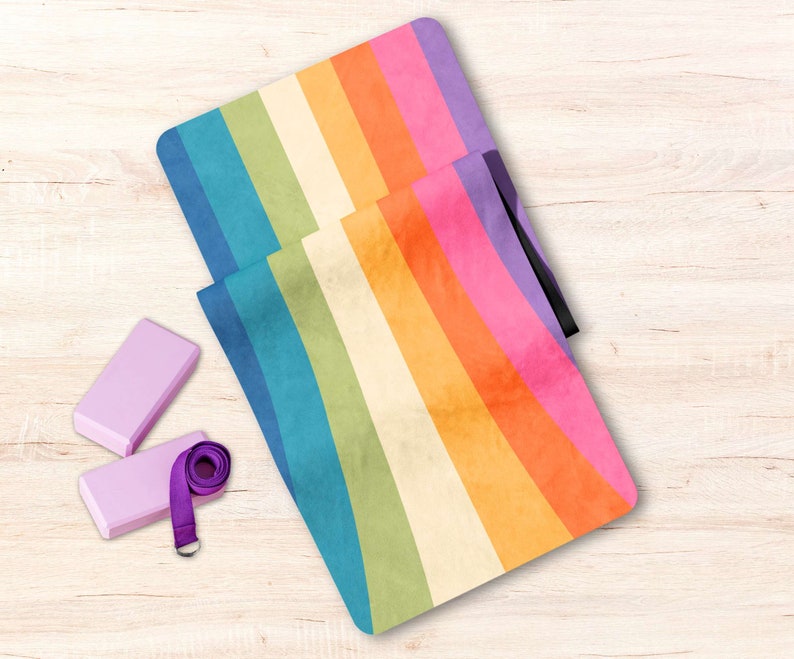 May include: A rainbow yoga mat with a purple strap and two purple yoga blocks. The mat has a faded, vintage look.