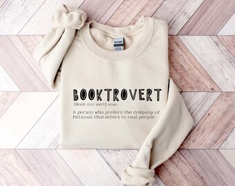 May include: A beige sweatshirt with the text "BOOKTROVERT [Book-tro-vert] noun A person who prefers the company of fictional characters to real people" printed on the front.
