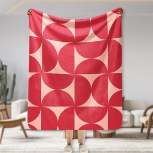 Pode incluir: Uma manta de arremesso com padrão geométrico vermelho e rosa com um padrão repetitivo de semicírculos.
