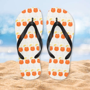 Puede incluir: Un par de chanclas blancas con una correa negra y un patrón de bebidas naranjas con rodajas de limón y pajitas.