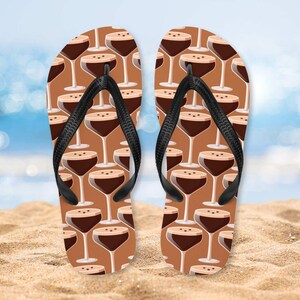 Könnte beinhalten: Ein Paar braune Flip-Flops mit schwarzem Riemen und einem Muster aus braunen und weißen Martini-Gläsern.